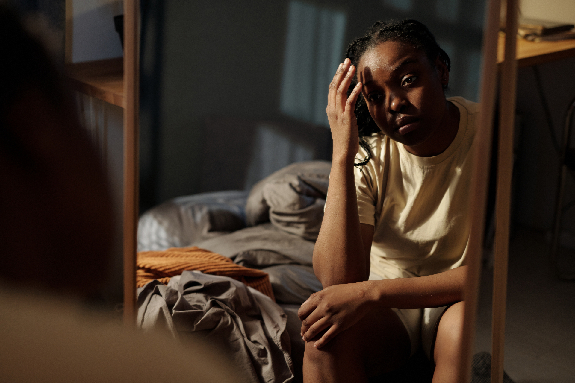 Vrouw zit alleen op de rand van een bed in een schaars verlichte kamer